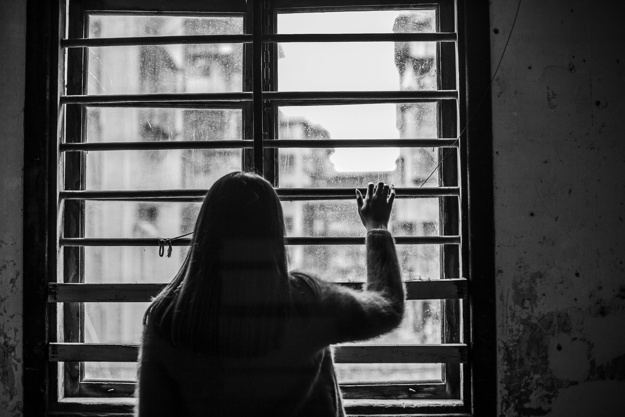 Back view of a teen girl looking out a window with bars