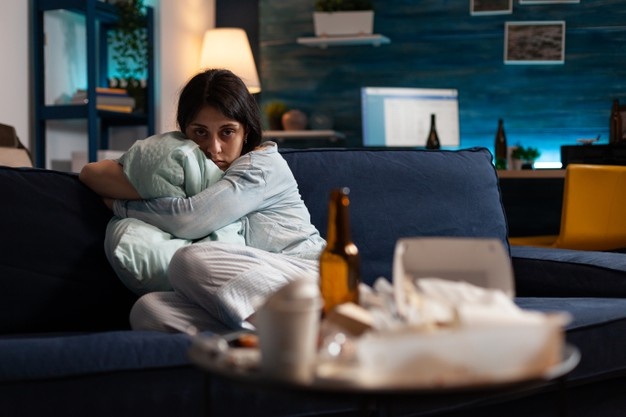 Sad teen girl hugging pillow on the couch after stress eating