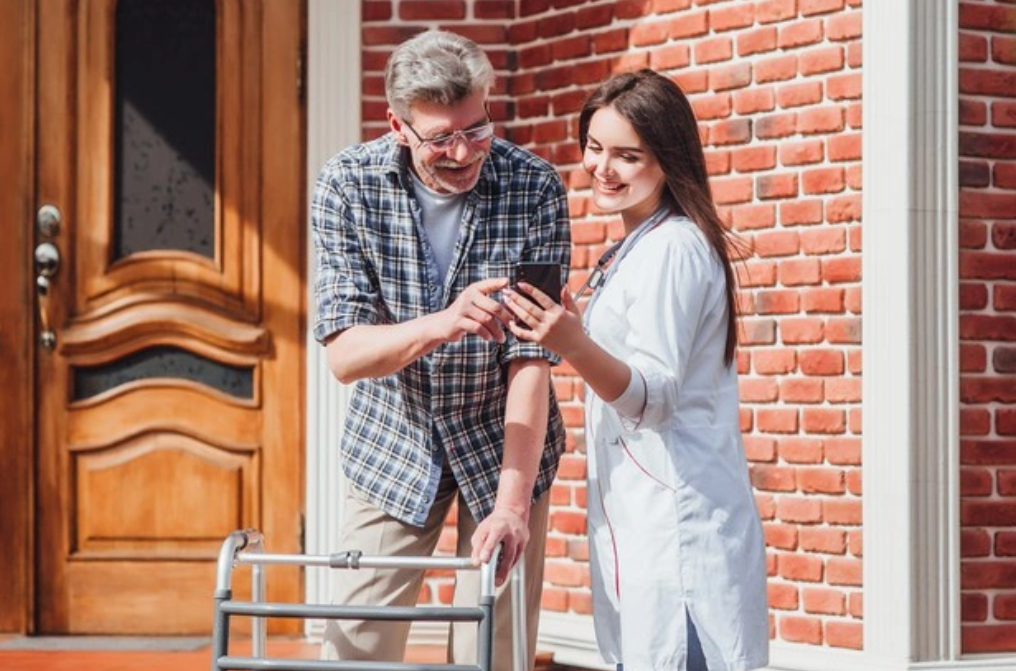 Senior man smiling and looking at smartphone held by caregiver