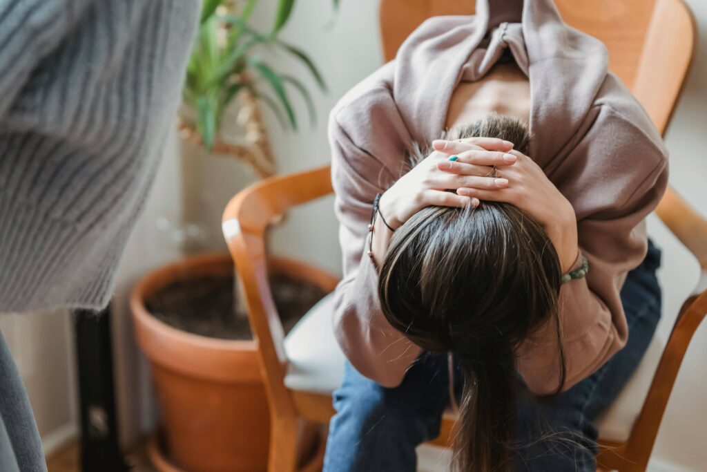 Person sitting on a chair with head bowed and hands covering face, appearing distressed